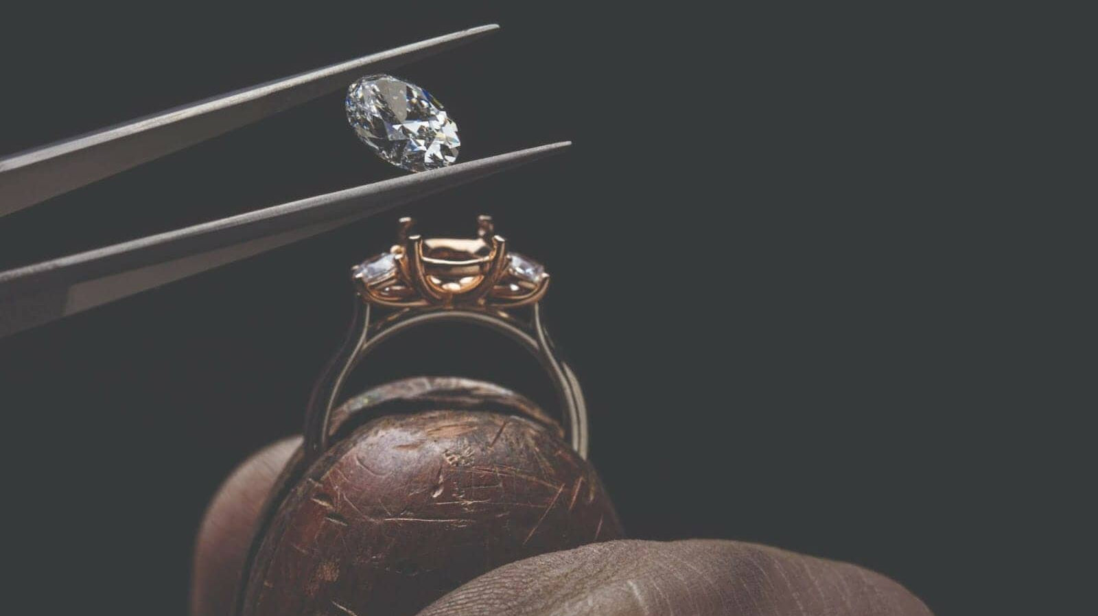 Diamond being set into a ring with tweezers against a black background