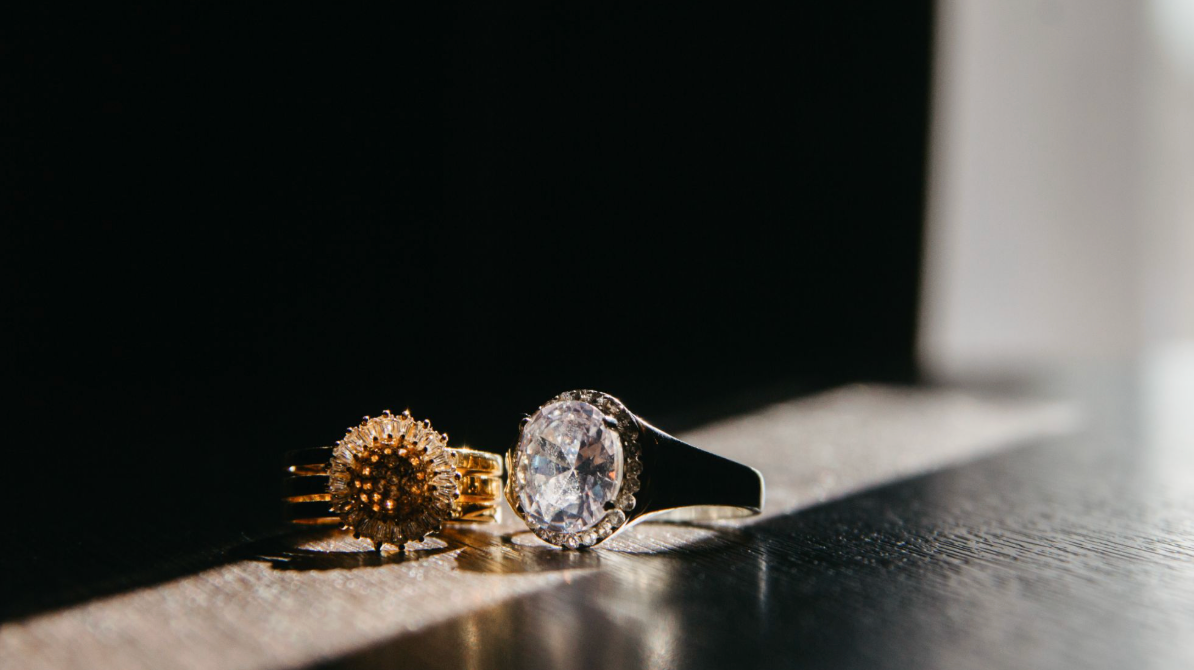 Two sparkling diamond rings resting on a dark wooden table in dramatic natural light.