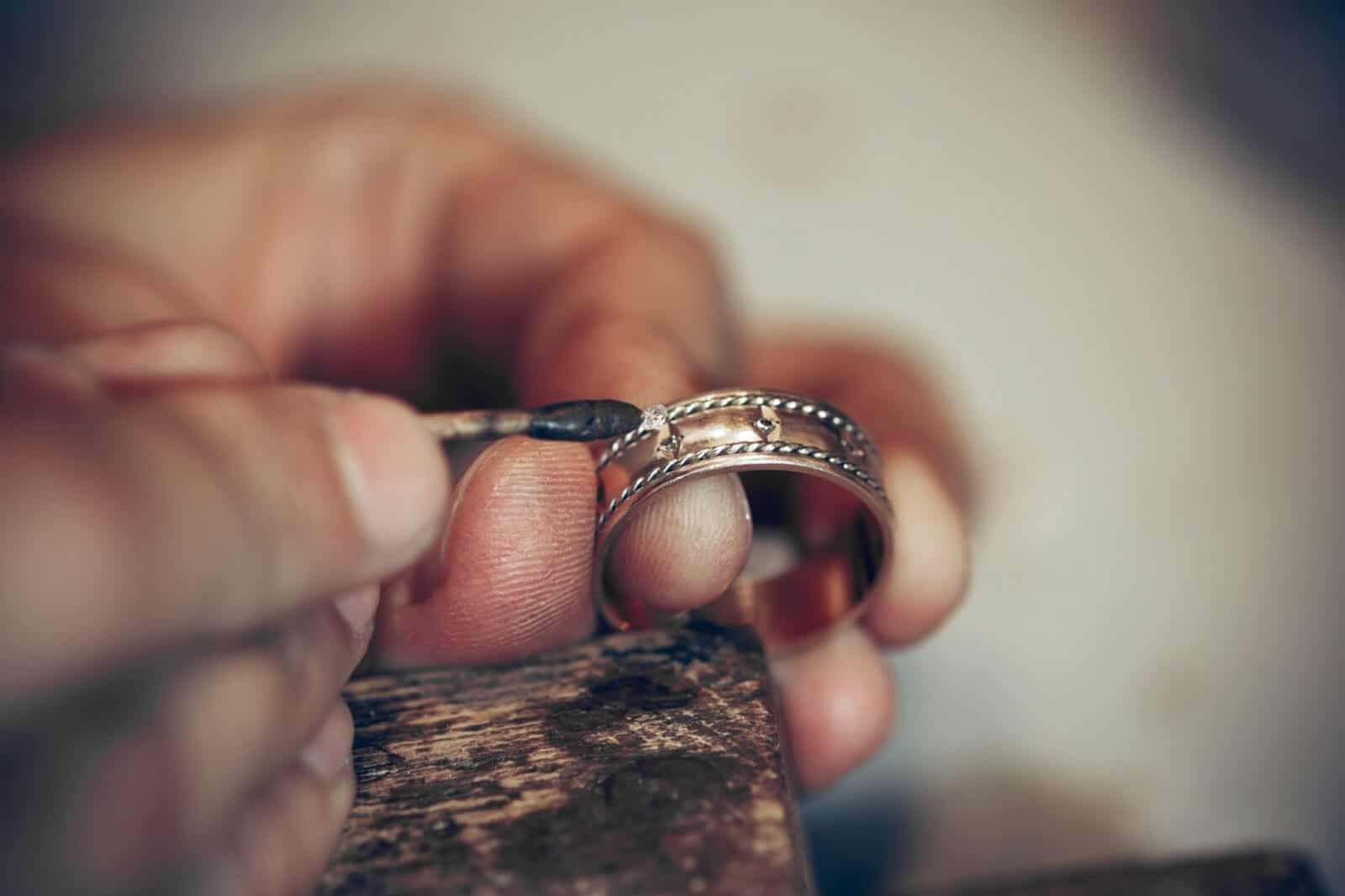 A workmans hands holding a piece of fine jewellery, gold ring and repairing a diamond on the ring which was damaged due to improper jewellery care