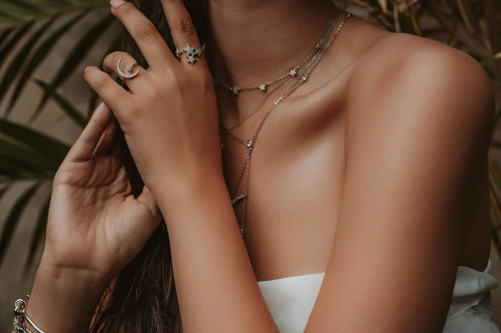 Close-up of a woman wearing layered 925 sterling silver jewellery, including star necklaces and celestial rings, showcasing the shine and craftsmanship of sterling silver pieces.