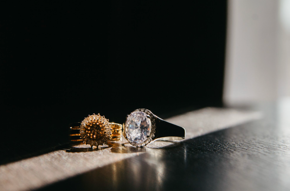 Two sparkling diamond rings resting on a dark wooden table in dramatic natural light.
