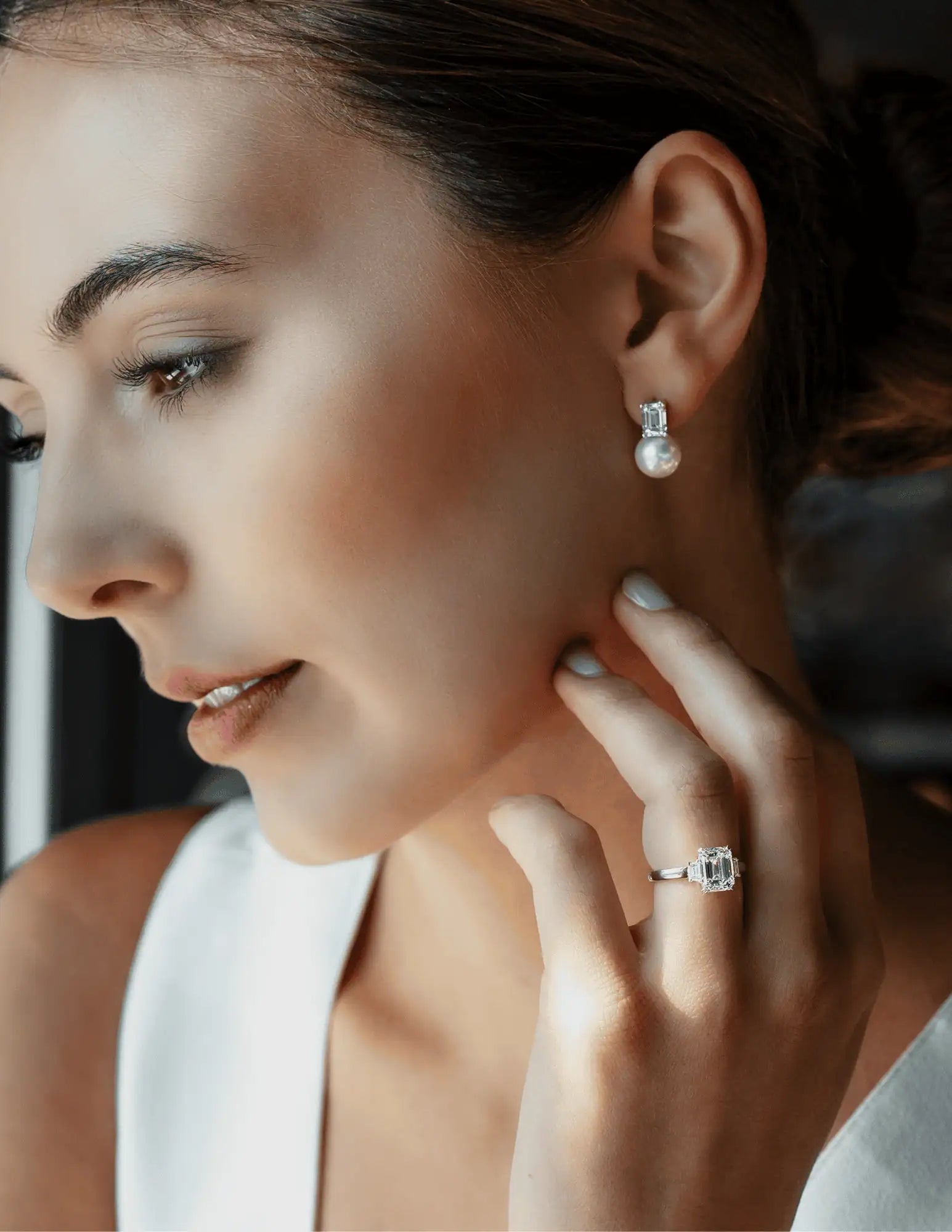 Close-up of a woman wearing an emerald-cut diamond engagement ring and pearl drop earrings with diamond accents.