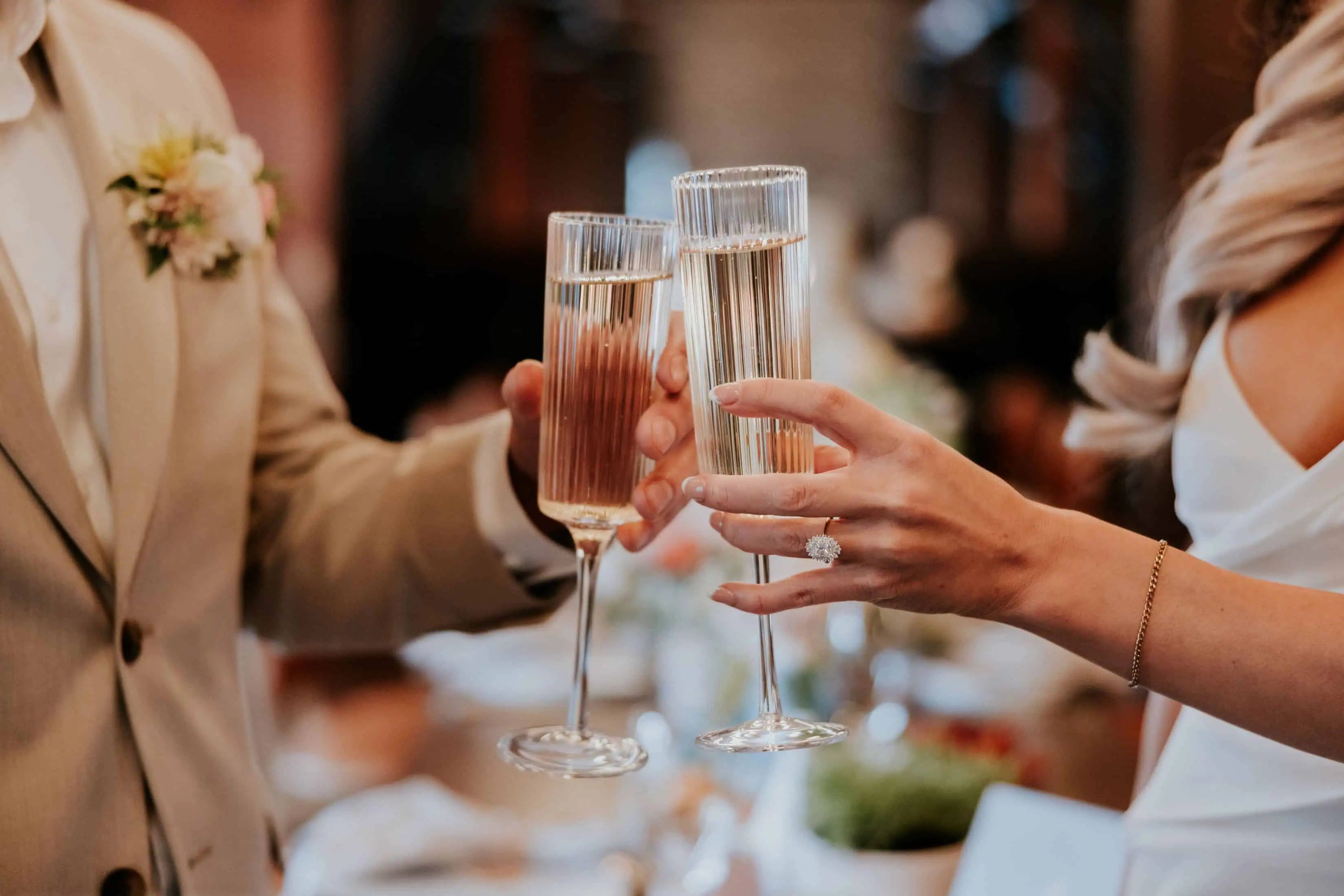 Bride and groom clinking champagne glasses during a wedding celebration, with the bride’s diamond engagement ring visible.