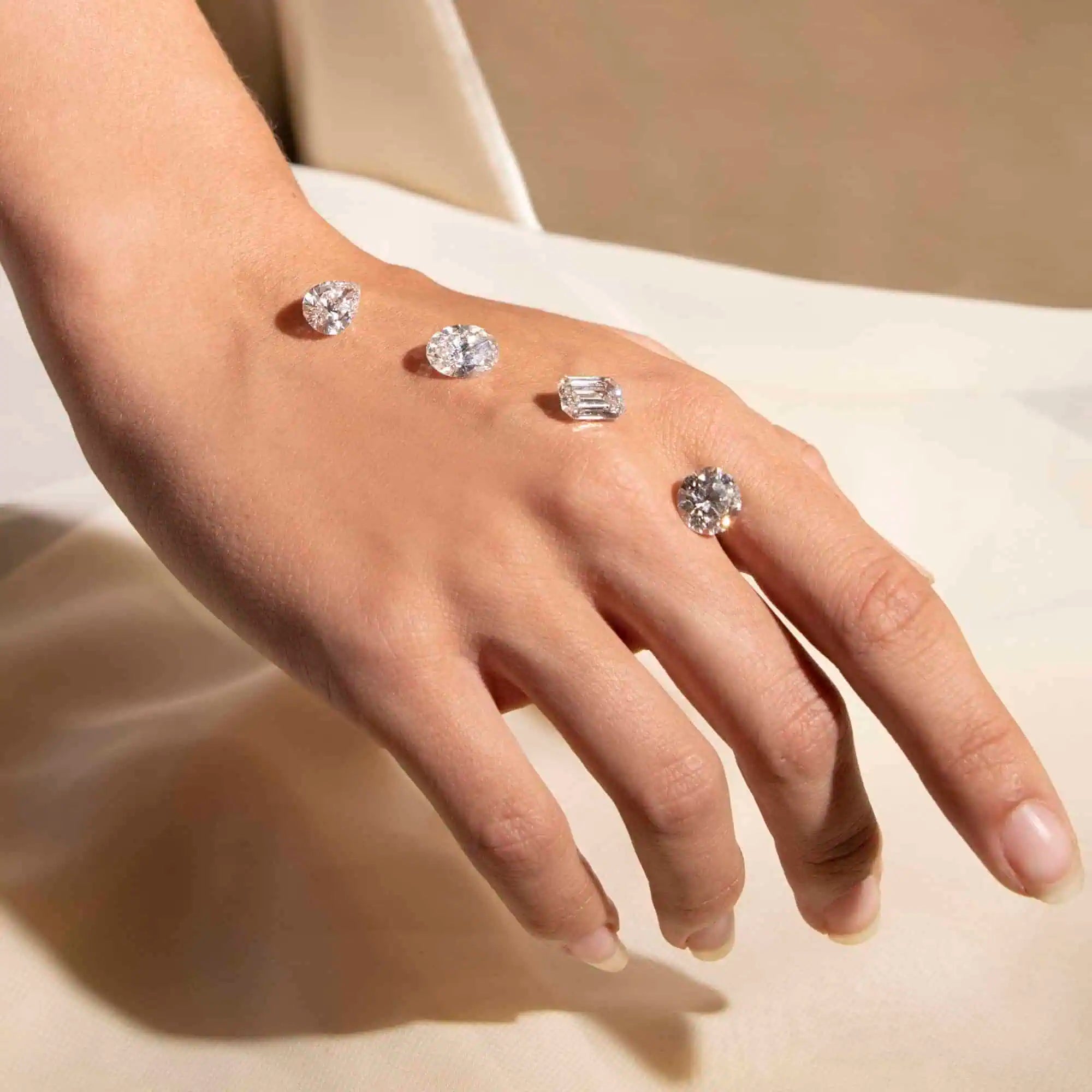 Hand displaying several loose diamonds in different cuts—including pear, oval, emerald, and round—arranged across the skin to showcase their brilliance and shape.