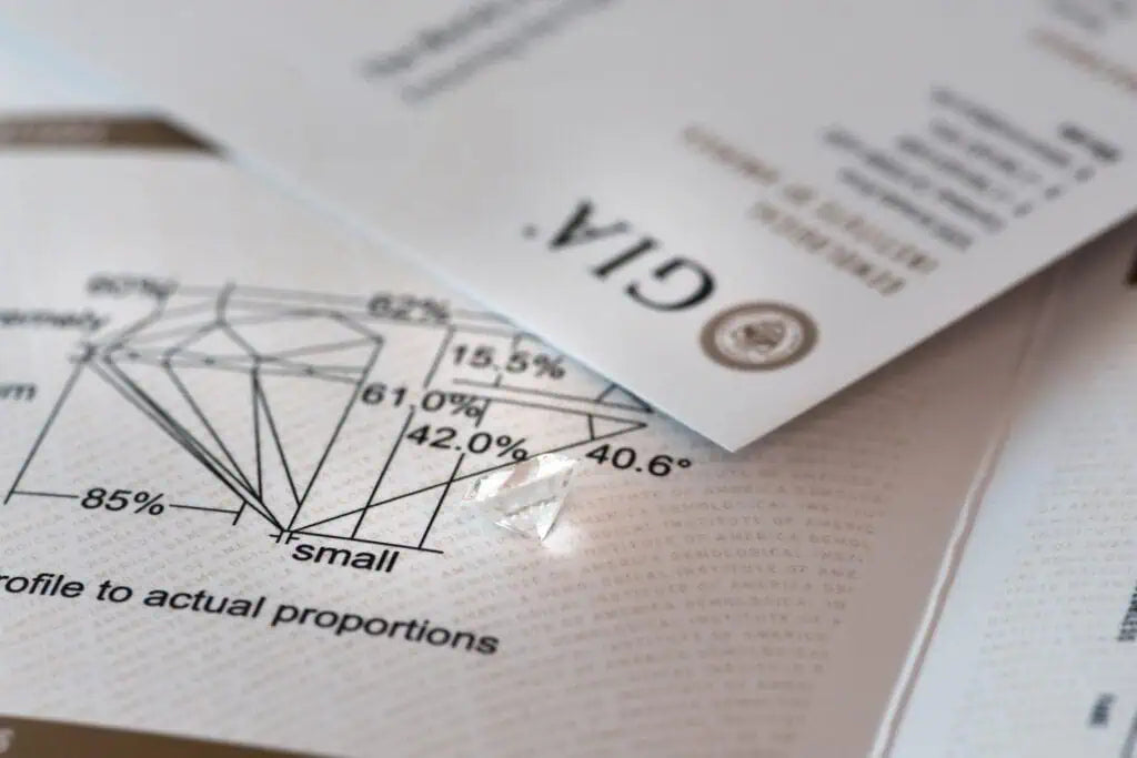 Loose diamond resting on a GIA grading report and diamond cut proportion diagram showing measurements and angles used to evaluate gemstone quality.