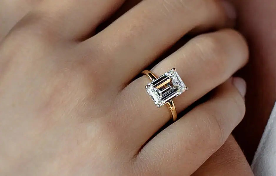 Close-up of an emerald-cut diamond engagement ring set in yellow gold, worn on a hand and highlighting the clean, step-cut facets of the center stone.