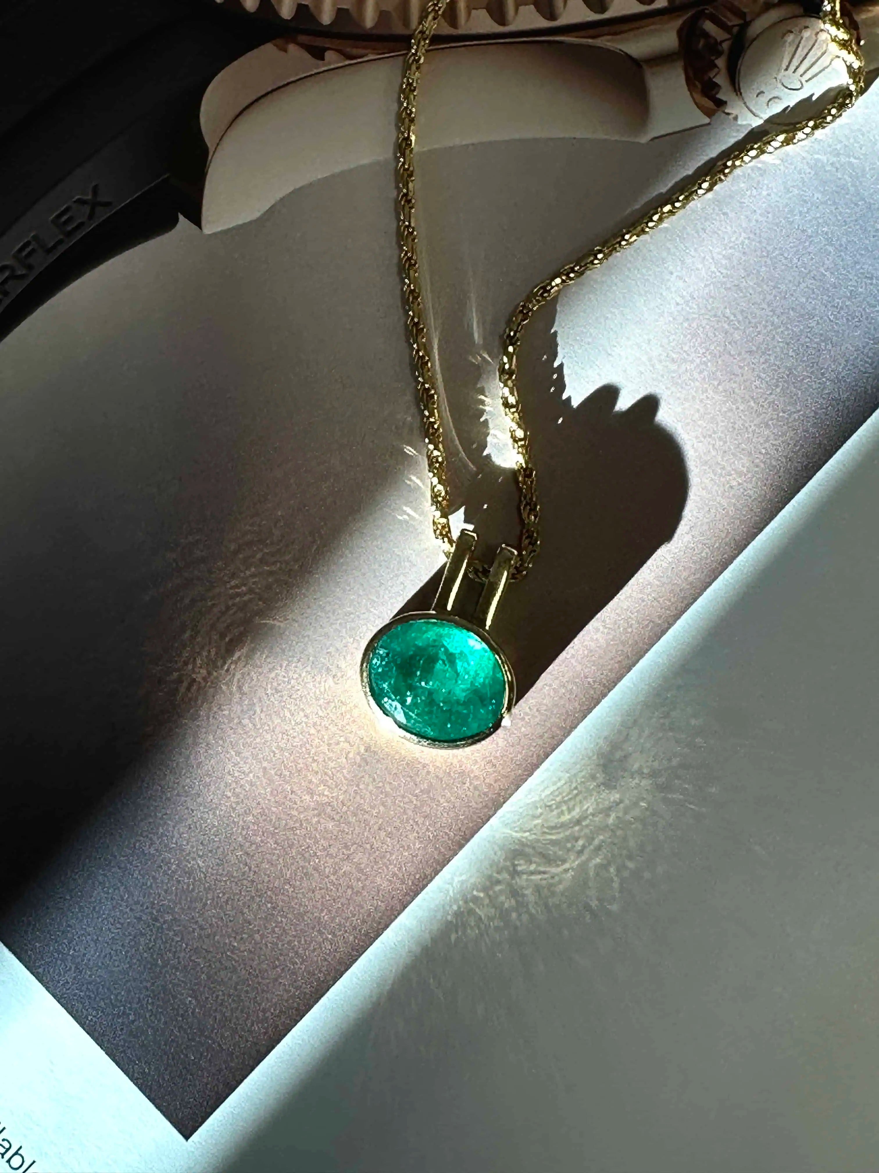 Gold pendant necklace with a vibrant green gemstone displayed on an open book, highlighting the stone’s rich color and brilliance in natural light.