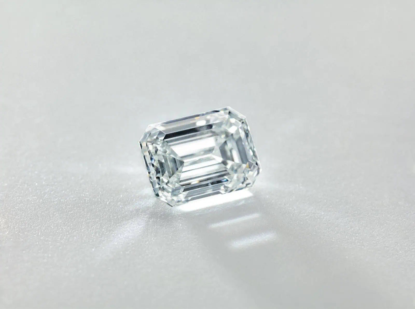 Loose emerald-cut diamond displayed on a neutral surface, highlighting the stone’s step-cut facets and clarity.