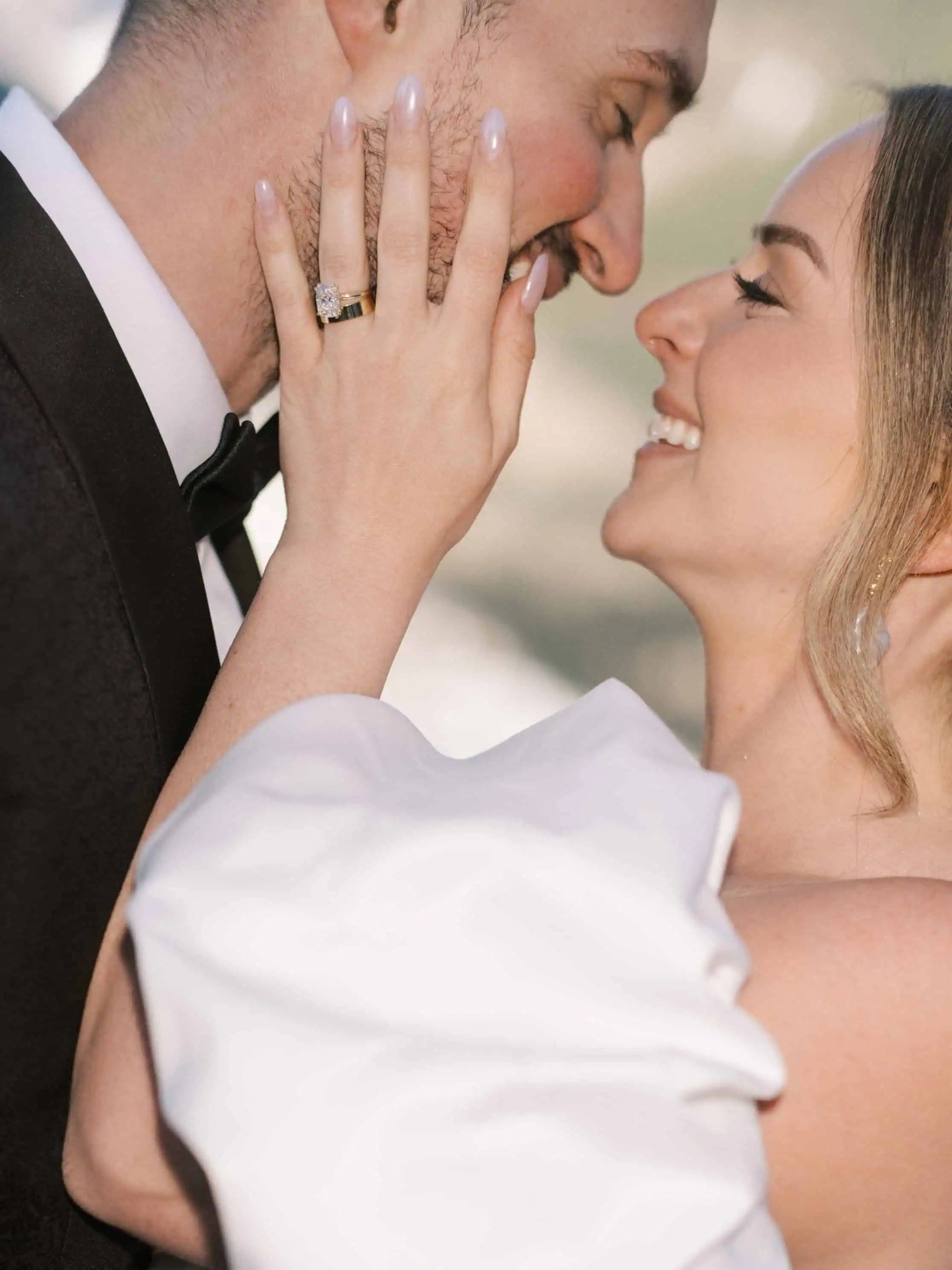 Bride gently touching groom’s face while showing a diamond engagement ring and wedding band, captured in a romantic wedding moment.