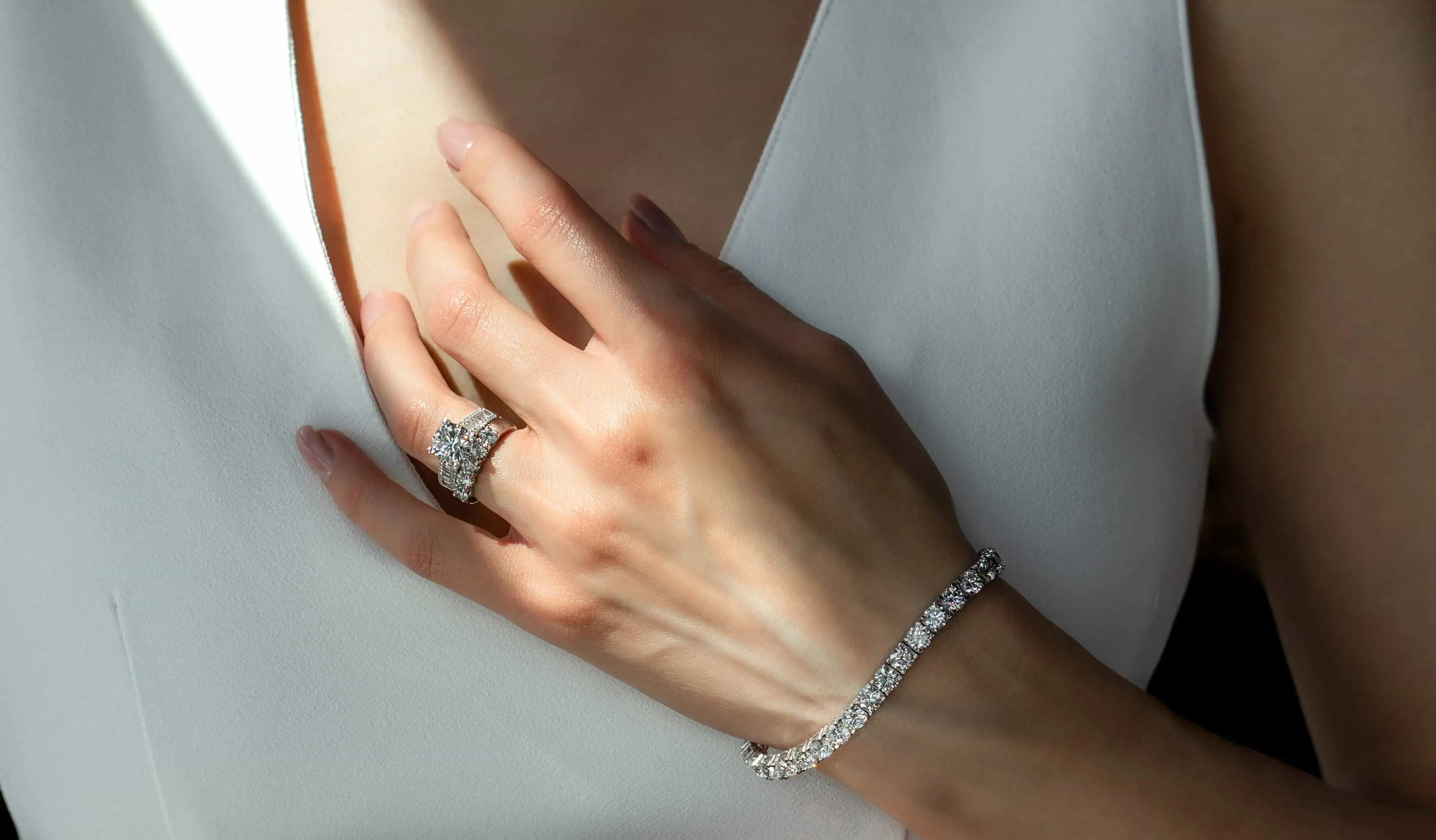 Close-up of a woman wearing a diamond engagement ring and matching diamond bracelet, styled against a white dress with soft lighting that highlights the sparkle and detail of the jewelry.
