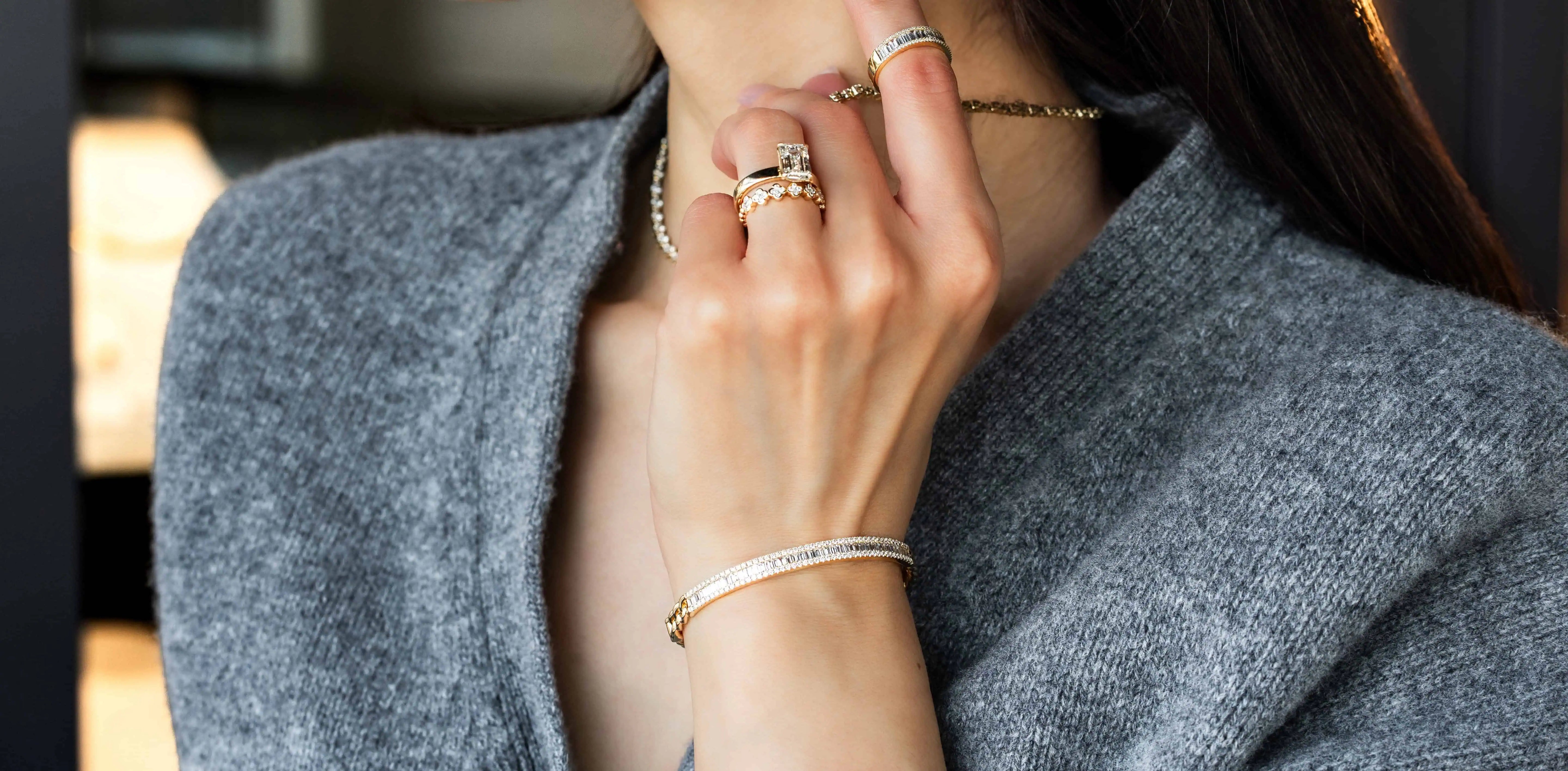 Close-up of a woman wearing stacked diamond rings, a diamond bracelet, and a delicate necklace, highlighting elegant fine jewelry styling.