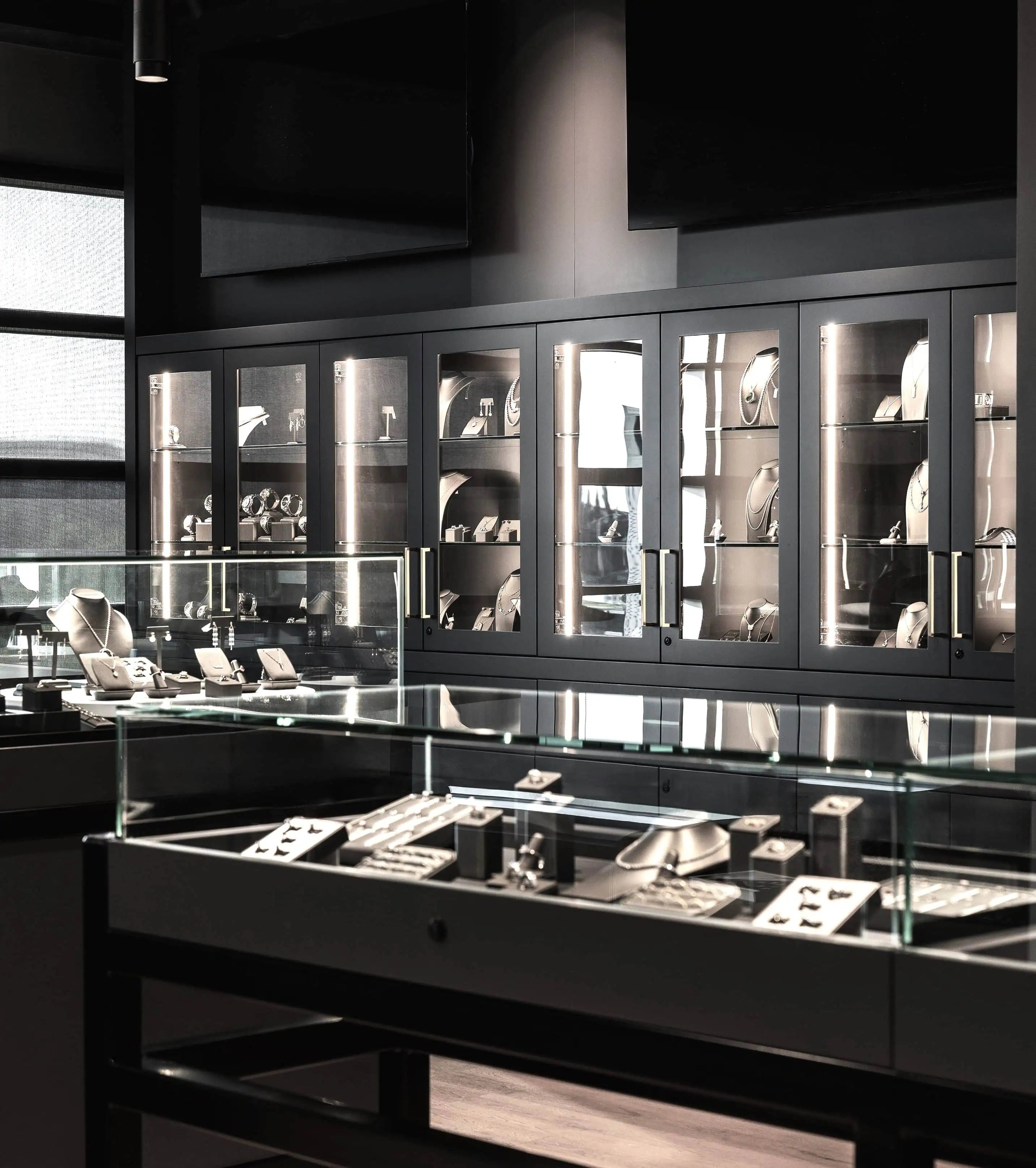 Modern luxury jewelry showroom featuring illuminated display cabinets and glass cases showcasing diamond rings, necklaces, and fine jewelry collections.